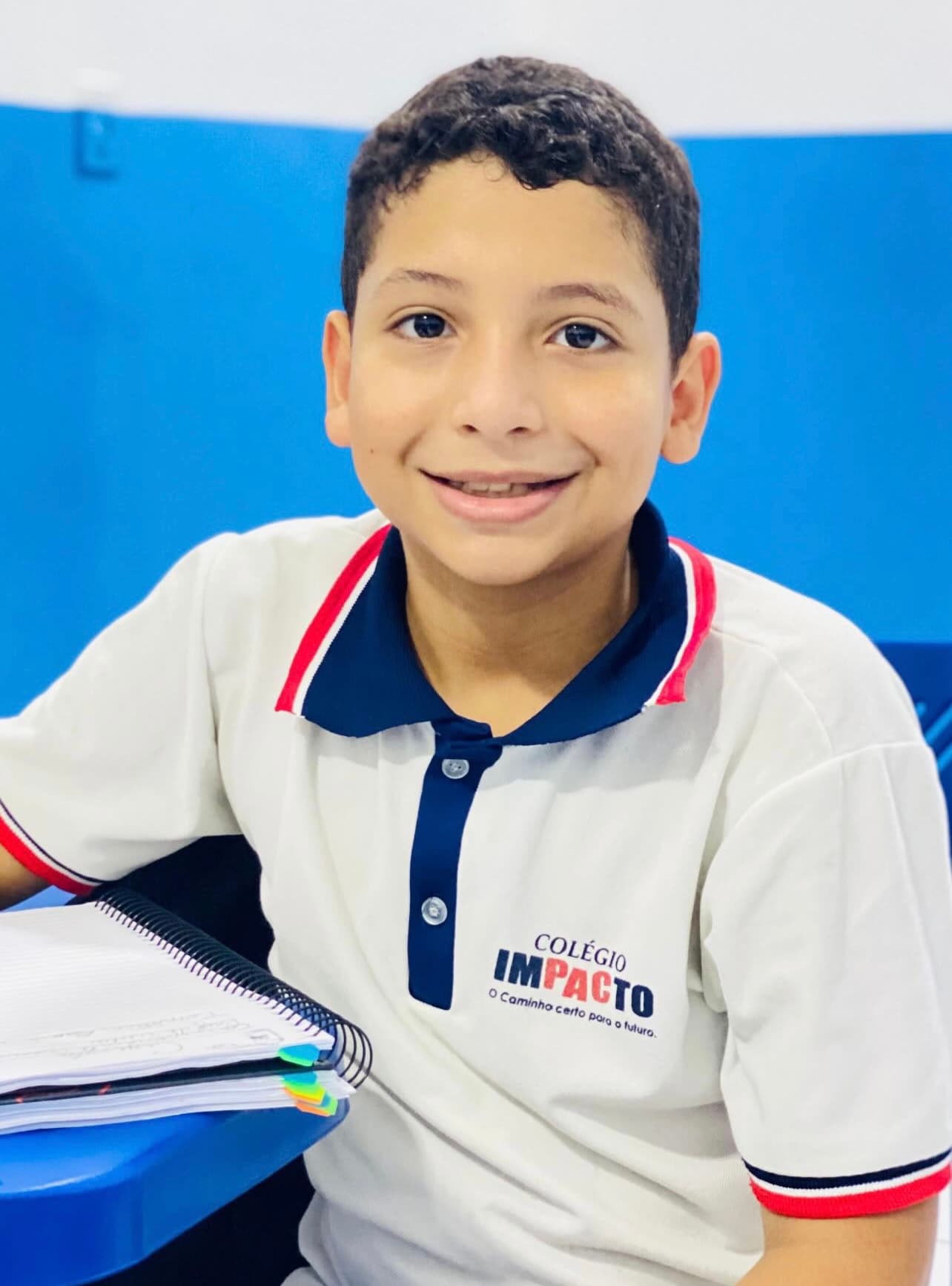 Aluno do Colégio Impacto sorrindo com seu caderno