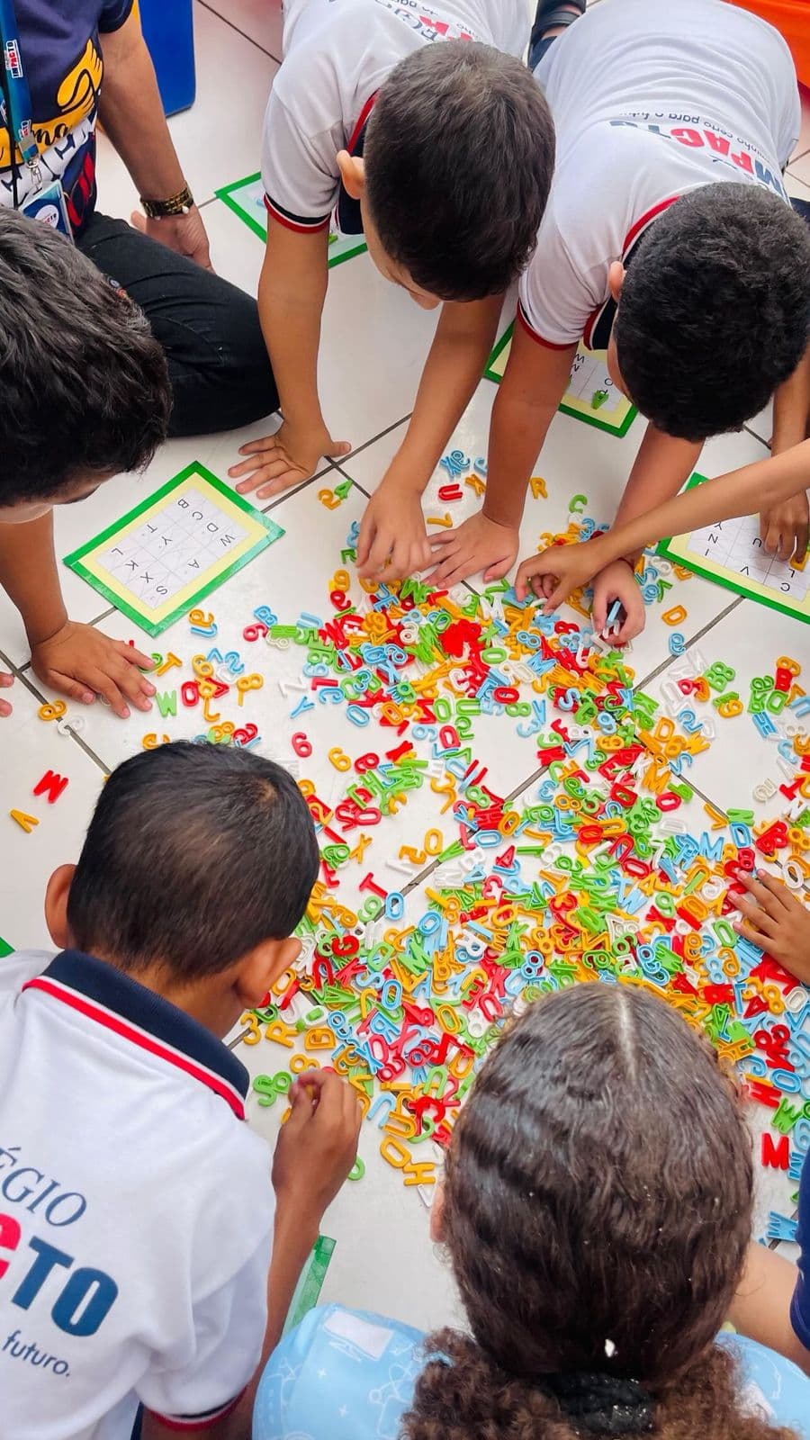 Alunos do Colégio Impacto brincando com letras e números no chão da sala